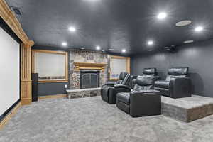Home theater with a stone fireplace, a textured ceiling, carpet floors, and recessed lighting