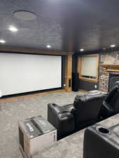 Carpeted cinema featuring a textured ceiling, recessed lighting, and a stone fireplace