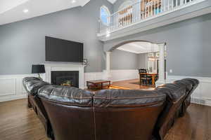 Living room with a tile fireplace, dark wood-style flooring, ornate columns, arched walkways, and a wainscoted wall