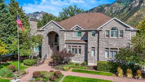 View of front facade with brick siding, a mountain view, a chimney, and roof with shingles