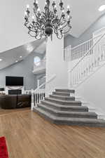 Staircase featuring wood finished floors, high vaulted ceiling, recessed lighting, and a chandelier