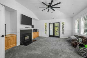Living room featuring dark colored carpet, a fireplace, lofted ceiling, a ceiling fan, and a decorative wall