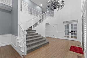 Foyer with a towering ceiling, french doors, a chandelier, stairs, and wood finished floors