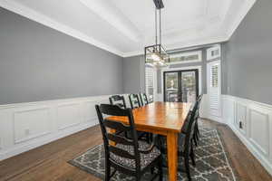 Dining room featuring wainscoting, a decorative wall, french doors, crown molding, and dark wood finished floors