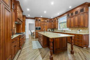 Kitchen with recessed lighting, tasteful backsplash, light wood finished floors, brown cabinetry, and light stone counters