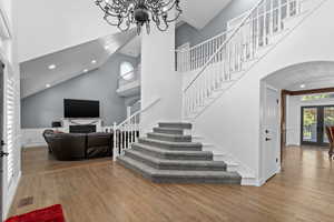 Entryway with stairway, arched walkways, wood finished floors, a chandelier, and high vaulted ceiling