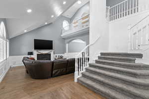 Living area with healthy amount of natural light, a fireplace, stairs, high vaulted ceiling, and wood finished floors