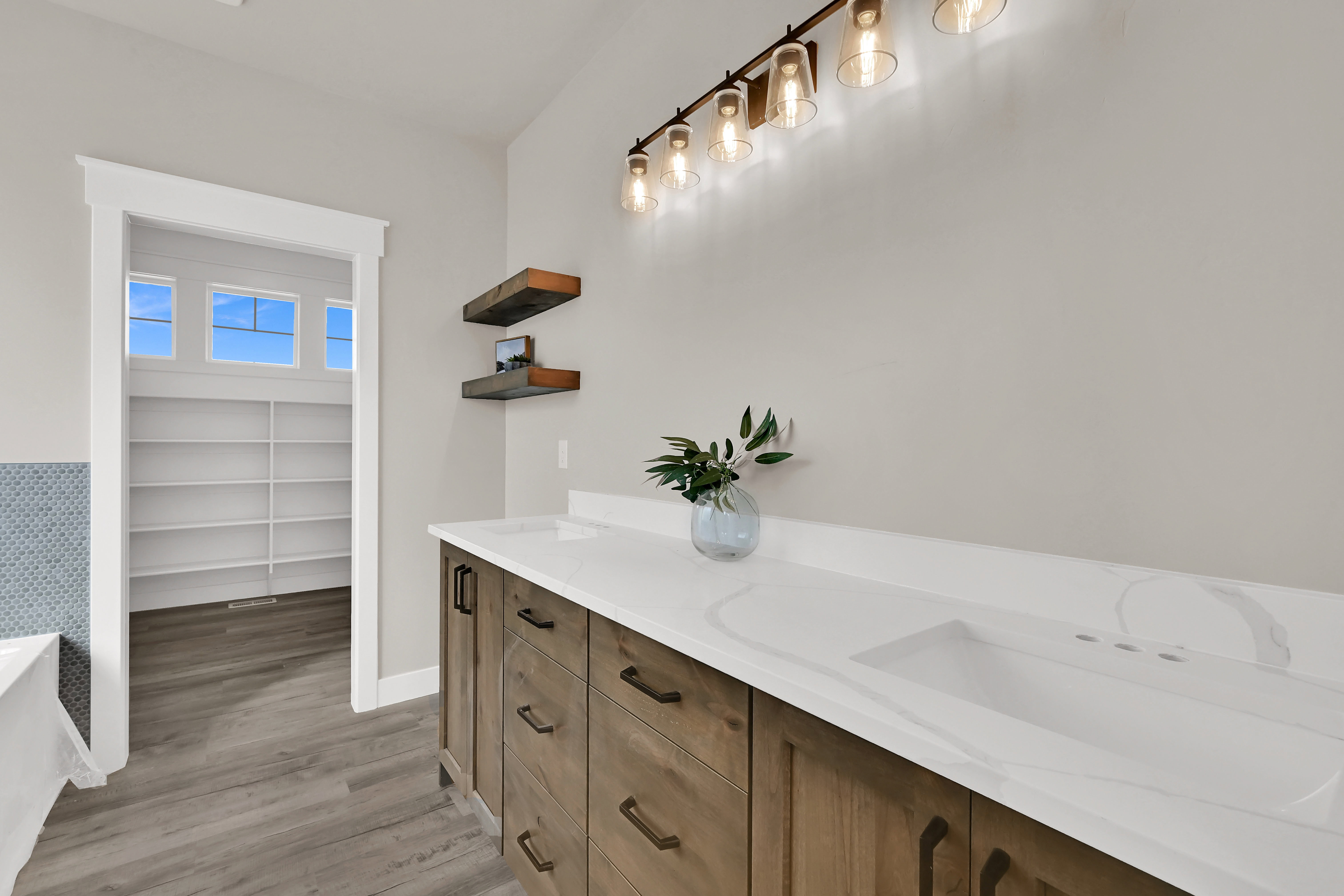 Full bath with double vanity, light wood-type flooring, a bathtub, and a walk in closet
