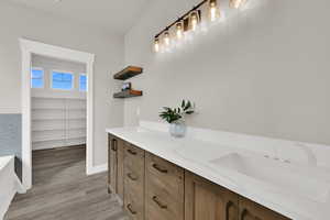 Full bath with double vanity, light wood-type flooring, a bathtub, and a walk in closet