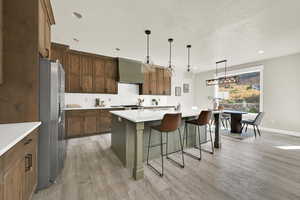 Kitchen featuring a center island with sink, pendant lighting, a kitchen breakfast bar, decorative backsplash, and light wood finished floors