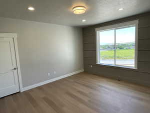 Empty room featuring a textured ceiling, light wood-style floors, and recessed lighting