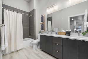 Bathroom with shower / bathtub combination with curtain, double vanity, and light wood-style floors