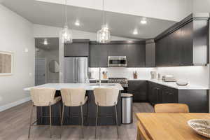 Kitchen featuring modern cabinets, lofted ceiling, decorative light fixtures, premium appliances, and a breakfast bar