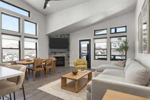 Living room featuring a fireplace, wood finished floors, high vaulted ceiling, and ceiling fan
