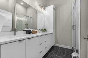 Full bathroom featuring a shower stall, double vanity, and dark marble finish flooring