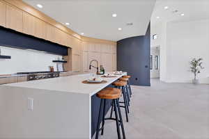 Kitchen featuring a kitchen breakfast bar, modern cabinets, a kitchen island with sink, light brown cabinets, and open shelves