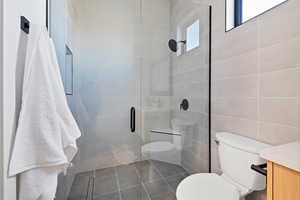 Bathroom featuring tile walls, a stall shower, dark tile patterned flooring, and vanity