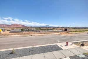View of asphalt road featuring a mountain view, sidewalks, and street lights