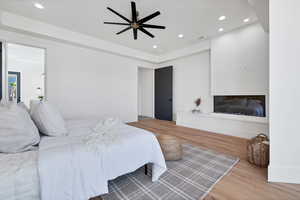 Bedroom featuring wood finished floors, recessed lighting, ceiling fan, and a glass covered fireplace