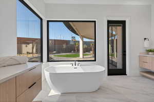 Bathroom featuring a freestanding bath, light marble finish flooring, and vanity