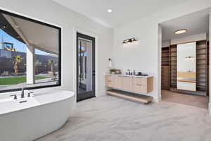 Full bath featuring vanity, a freestanding bath, light marble finish flooring, recessed lighting, and a walk in closet