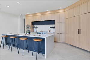Kitchen featuring light brown cabinetry, a kitchen bar, modern cabinets, recessed lighting, and decorative backsplash