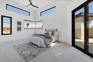 Carpeted bedroom with access to exterior, ceiling fan, and a high ceiling