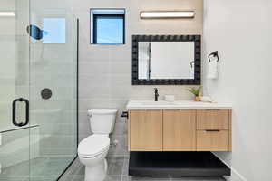 Bathroom with tile walls, vanity, dark tile patterned flooring, and a shower stall