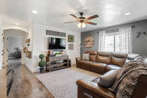 Living room featuring a textured ceiling, wood finished floors, ceiling fan, arched walkways, and recessed lighting