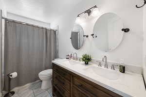 Full bath featuring double vanity, a shower with curtain, a textured ceiling, and light marble finish flooring