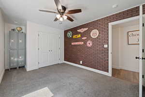 Unfurnished bedroom with carpet floors, a closet, ceiling fan, and brick wall