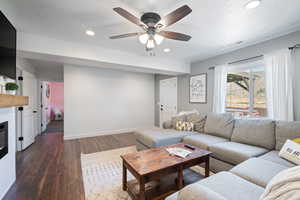 Living area featuring dark wood-type flooring, a ceiling fan, recessed lighting, a glass covered fireplace, and a textured ceiling
