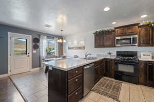 Kitchen featuring dark brown cabinetry, appliances with stainless steel finishes, a textured ceiling, a chandelier, and a peninsula