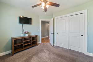 Carpeted bedroom with ceiling fan, a closet, and a textured ceiling