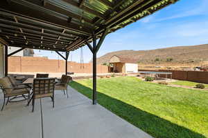 Fenced backyard featuring a patio area, a mountain view, a storage unit, outdoor dining area, and a trampoline