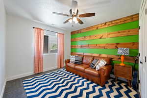 Carpeted living room with a textured ceiling, wood walls, and ceiling fan