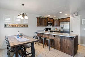 Kitchen featuring dark brown cabinetry, appliances with stainless steel finishes, a peninsula, pendant lighting, and a breakfast bar area