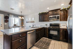 Kitchen featuring dark brown cabinetry, stainless steel appliances, a peninsula, a textured ceiling, and a chandelier
