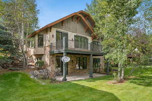 Rear view of house featuring a yard, stone siding, stucco siding, and a patio