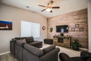 Living area with an accent wall, wooden walls, wood tiled floors, a ceiling fan, and vaulted ceiling