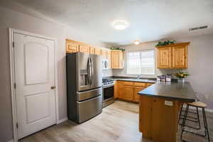 Kitchen with dark countertops, stainless steel appliances, a peninsula, a kitchen bar, and a textured ceiling