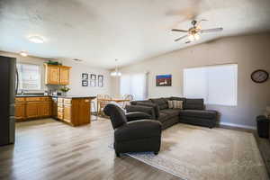 Living room featuring light wood-style flooring, ceiling fan, a textured ceiling, a chandelier, and vaulted ceiling