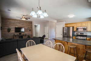 Dining space featuring wooden walls, an accent wall, a chandelier, light wood finished floors, and ceiling fan