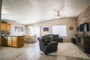 Living area featuring healthy amount of natural light, light wood-style floors, a textured ceiling, a ceiling fan, and vaulted ceiling