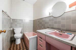 Bathroom with tile walls, a garden tub, vanity, and wainscoting