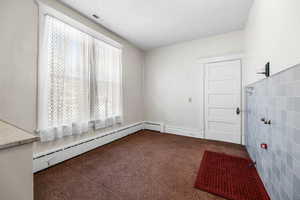 Carpeted empty room with baseboard heating, a textured ceiling, and tile walls