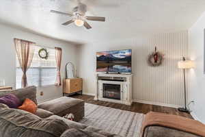 Living room with a glass covered fireplace, dark wood finished floors, wallpapered walls, a textured ceiling, and an accent wall