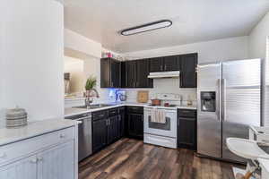 Kitchen with stainless steel appliances, backsplash, dark wood-style floors, a textured ceiling, and dark cabinetry