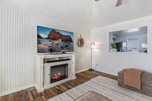 Living room with wallpapered walls, dark wood-style floors, a textured ceiling, a glass covered fireplace, and ceiling fan