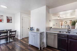 Kitchen featuring a textured ceiling, stainless steel dishwasher, light countertops, dark wood-style floors, and a ceiling fan